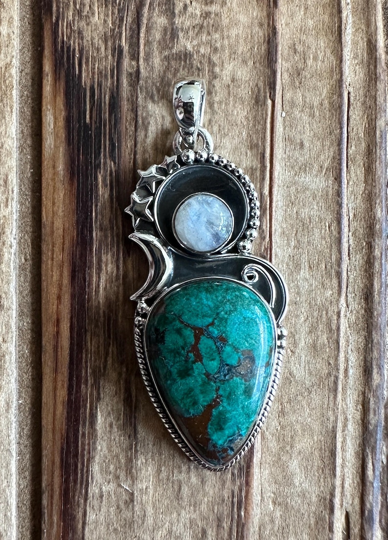 May include: A silver pendant with a green turquoise stone and a moonstone. The pendant is set in a silver frame with a crescent moon design and stars.
