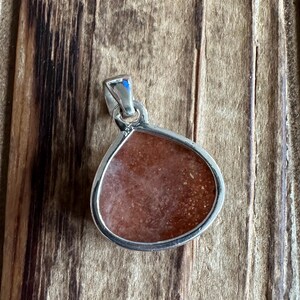 May include: A teardrop-shaped pendant with a silver setting and a red-brown stone.