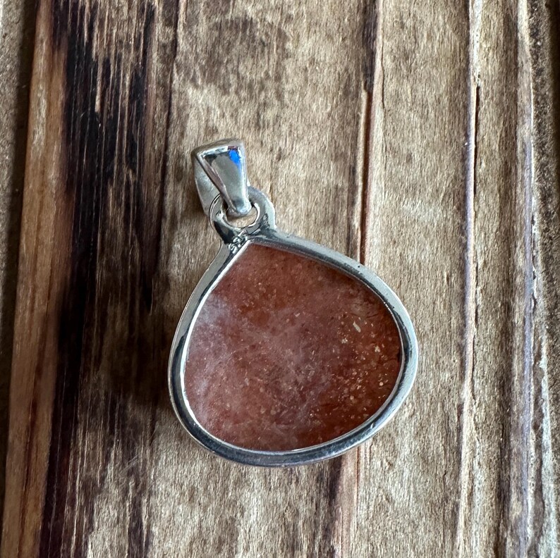 May include: A teardrop-shaped pendant with a silver setting and a red-brown stone.