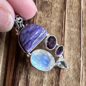 May include: A silver pendant with a large purple and blue gemstone, surrounded by smaller amethyst and moonstone gemstones.