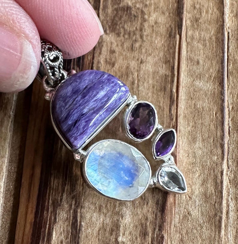 May include: A silver pendant with a large purple and blue gemstone, surrounded by smaller amethyst and moonstone gemstones.
