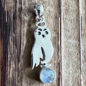 May include: Silver owl pendant featuring a moonstone cabochon. The owl is detailed with eyes and a halo. The moonstone is iridescent.