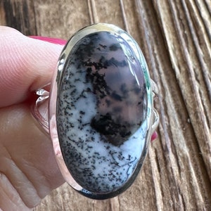 May include: A silver ring with a large oval-shaped black and white agate stone. The stone has a swirling pattern of black and white.