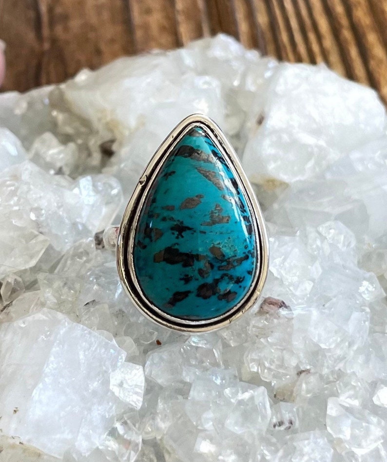 May include: A teardrop-shaped turquoise ring set in sterling silver. The turquoise is a deep blue-green color with black and brown veins.