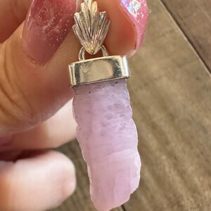 Puede incluir: Un colgante de plata con un cristal rosa. El cristal es de forma natural y tiene un color rosa claro.