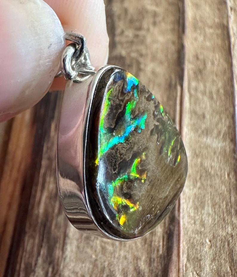 May include: A silver pendant with a teardrop-shaped opal stone. The opal has a dark gray base with iridescent green, blue, and yellow flashes.