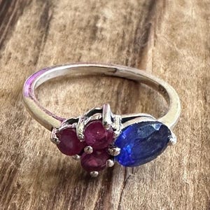 May include: A silver ring with a cluster of red gemstones and a single blue gemstone.