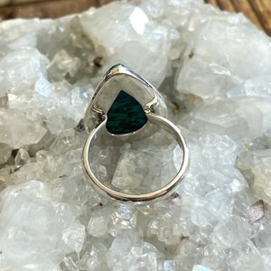 May include: A silver ring with a teardrop-shaped turquoise stone set in the center. The ring is on a white background.