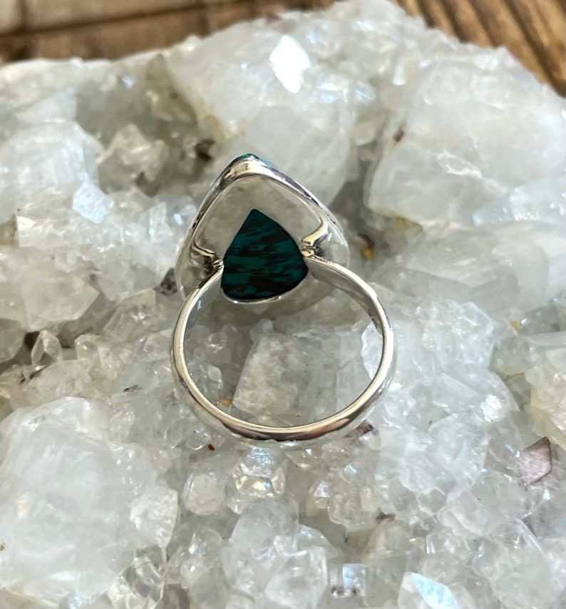 May include: A silver ring with a teardrop-shaped turquoise stone set in the center. The ring is on a white background.