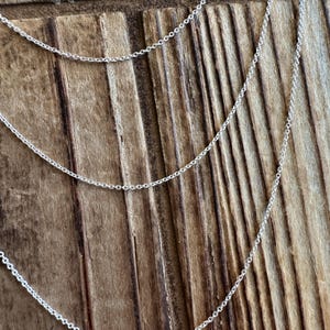 May include: Three silver chains of varying lengths on a wooden background.
