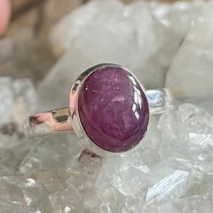 May include: A silver ring with a large oval-shaped pink gemstone. The ring is set on a bed of white crystals.