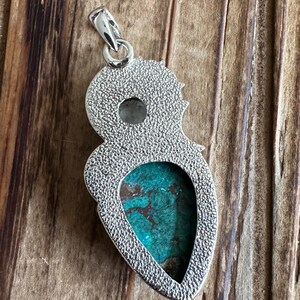 May include: Silver pendant with a turquoise stone set in a teardrop shape. The pendant has a textured surface and a loop at the top for attaching a chain.