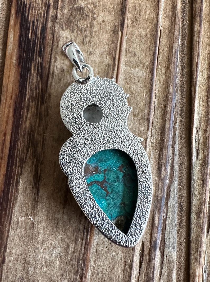 May include: Silver pendant with a turquoise stone set in a teardrop shape. The pendant has a textured surface and a loop at the top for attaching a chain.