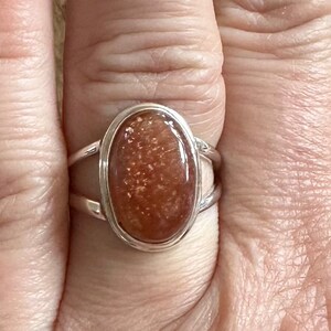 May include: A silver ring with an oval-shaped sunstone. The sunstone is a deep orange color with a shimmery, glittery texture.