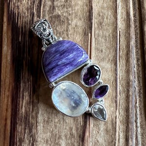 May include: A silver pendant with a purple and white gemstone cluster. The pendant features a large, purple, semi-circular stone, a smaller, round, white stone, and three smaller, purple stones.