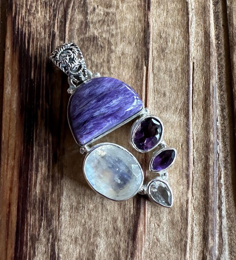 May include: A silver pendant with a purple and white gemstone cluster. The pendant features a large, purple, semi-circular stone, a smaller, round, white stone, and three smaller, purple stones.