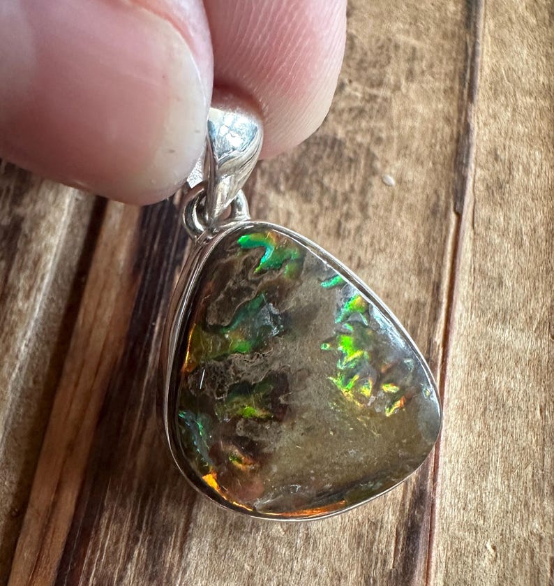 May include: A silver pendant with a dark brown, green, and iridescent opal stone. The stone is set in a silver bezel and has a teardrop shape.