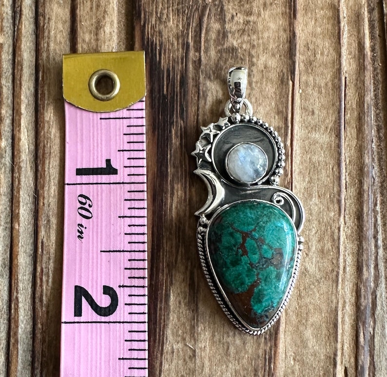 May include: A silver pendant with a green and brown turquoise stone and a moonstone. The pendant is about 2 inches long.