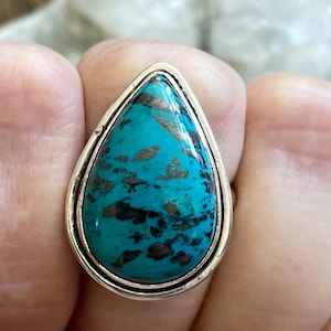May include: A silver ring with a teardrop-shaped turquoise stone. The stone has a mottled pattern of black and blue.