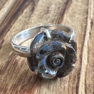 May include: A silver ring with a blue and black opal rose design.