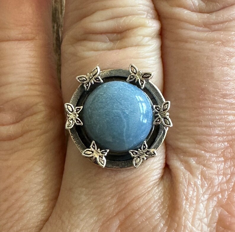 May include: A silver ring with a blue stone surrounded by butterfly designs.