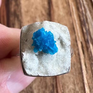 May include: A silver ring with a blue crystal set in a white stone. The crystal is a cluster of small, sharp points.