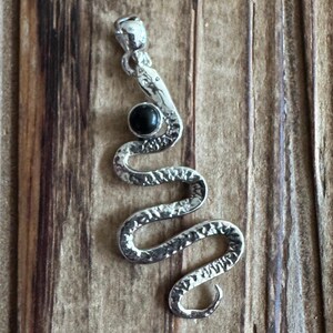 May include: Silver snake pendant with a black gemstone. The snake is coiled and has a textured surface.