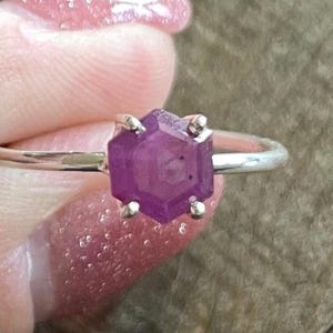 May include: A silver ring with a purple hexagonal gemstone.