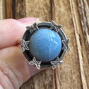 May include: A silver ring with a blue stone set in a circular bezel. The bezel is decorated with six silver butterfly designs.