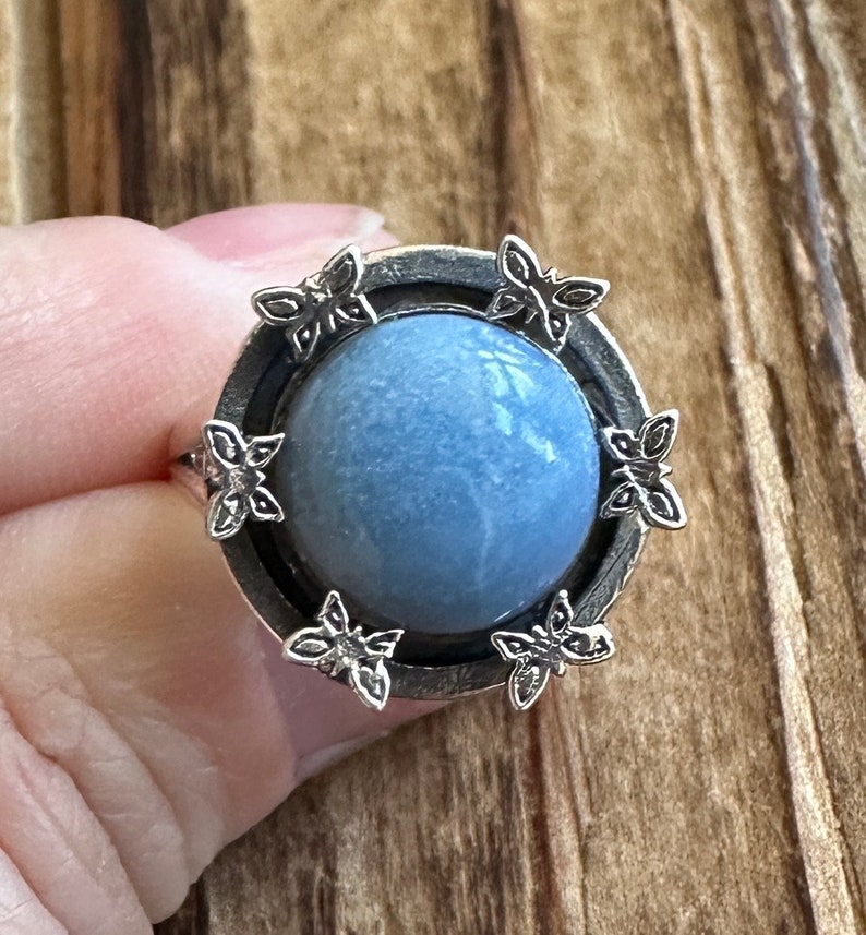 May include: A silver ring with a blue stone set in a circular bezel. The bezel is decorated with six silver butterfly designs.