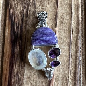 May include: A silver pendant with a large purple and blue gemstone, surrounded by smaller white and purple gemstones.