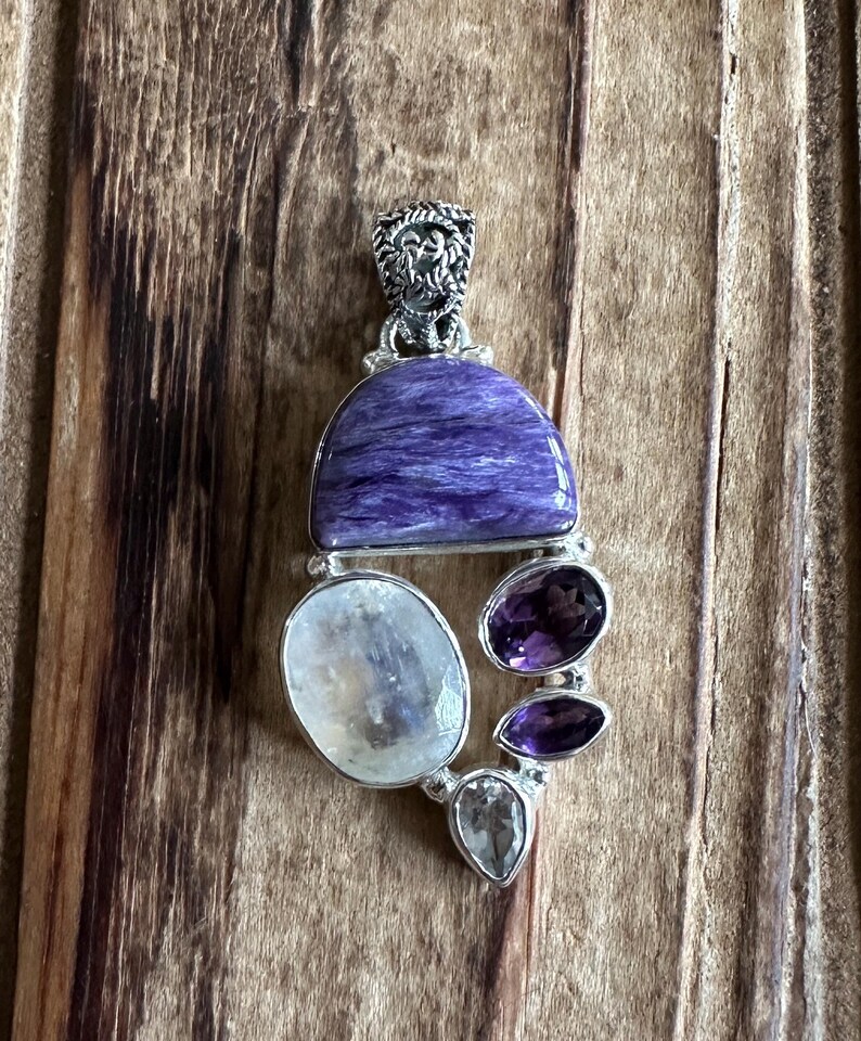 May include: A silver pendant with a large purple and blue gemstone, surrounded by smaller white and purple gemstones.