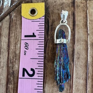 May include: A silver pendant featuring a iridescent blue and purple crystal with a silver bail. The pendant is approximately 2 inches long.