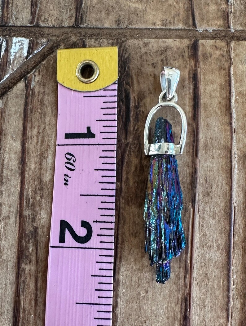 May include: A silver pendant featuring a iridescent blue and purple crystal with a silver bail. The pendant is approximately 2 inches long.