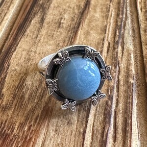May include: A silver ring with a blue gemstone set in a circular design with floral accents.