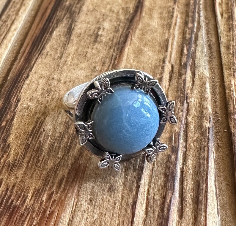 May include: A silver ring with a blue gemstone set in a circular design with floral accents.