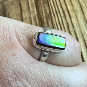 K&ouml;nnte beinhalten: Ein silberner Ring mit einem rechteckigen, schillernden Edelstein. Der Edelstein hat Blaut&ouml;ne, Gr&uuml;nt&ouml;ne und Gelbt&ouml;ne.