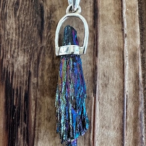 May include: A silver pendant featuring a iridescent blue, purple, and green crystal. The crystal is set in a silver bail.