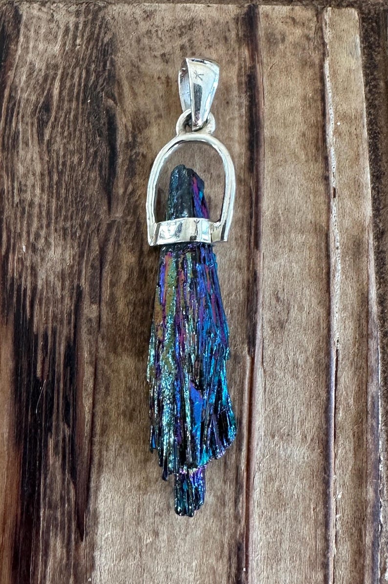 May include: A silver pendant featuring a iridescent blue, purple, and green crystal. The crystal is set in a silver bail.