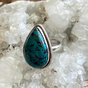 May include: A teardrop-shaped turquoise ring set in sterling silver. The turquoise is a deep blue-green color with black and white veins.