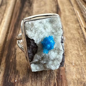 May include: A silver ring with a rectangular blue and white crystal stone set in the center.