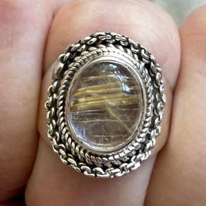 Pu&ograve; includere: Anello d'argento ovale con una gemma trasparente con inclusioni dorate. La gemma &egrave; incastonata in una montatura d'argento decorativa con un bordo a catena. Questo anello &egrave; un gioiello, adatto per l'uso quotidiano o per occasioni speciali.
