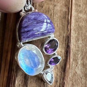 May include: A silver pendant with a large purple and white gemstone, surrounded by smaller purple gemstones.