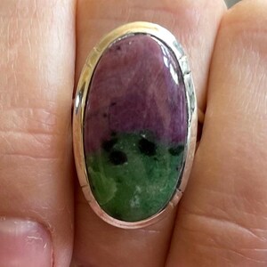 May include: A silver ring with an oval-shaped green and purple gemstone. The gemstone has a mottled pattern.