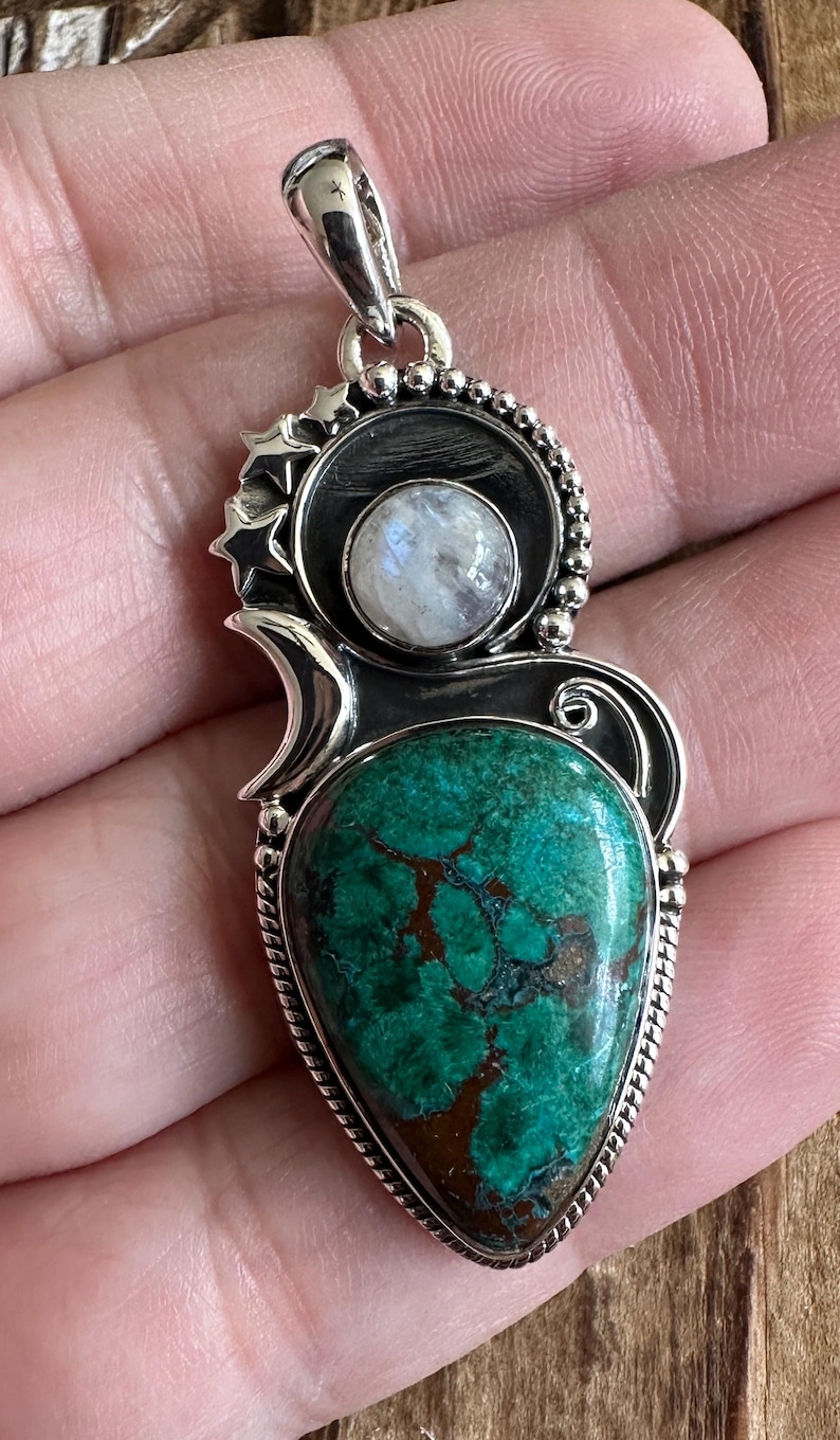 May include: A silver pendant with a green and brown gemstone, a round moonstone, and a star design.