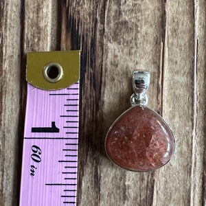 May include: A silver pendant with a reddish-brown sunstone gemstone. The pendant is approximately 1 inch in length.