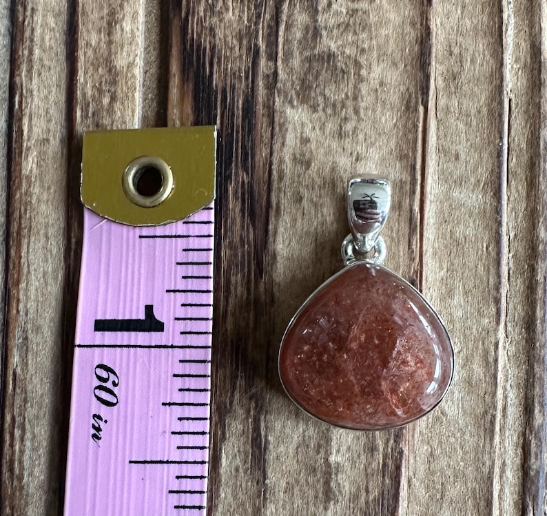 May include: A silver pendant with a reddish-brown sunstone gemstone. The pendant is approximately 1 inch in length.