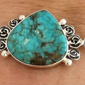 May include: A silver bracelet with a turquoise stone and rose-shaped accents.