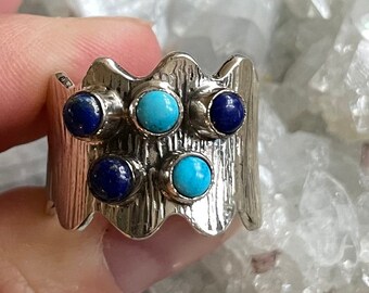 May include: A silver ring with a wavy band and five gemstones. Three of the gemstones are turquoise and two are lapis lazuli.