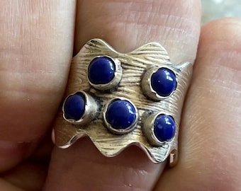May include: A silver ring with a wavy band and five blue gemstones set into the metal.